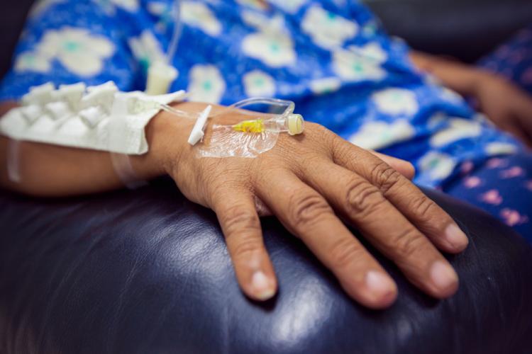 Close-up of the hand of a patient with a drip inserted - they are receiving chemotherapy. The patient&#039;s hand rests on the arm of a black leather armchair.